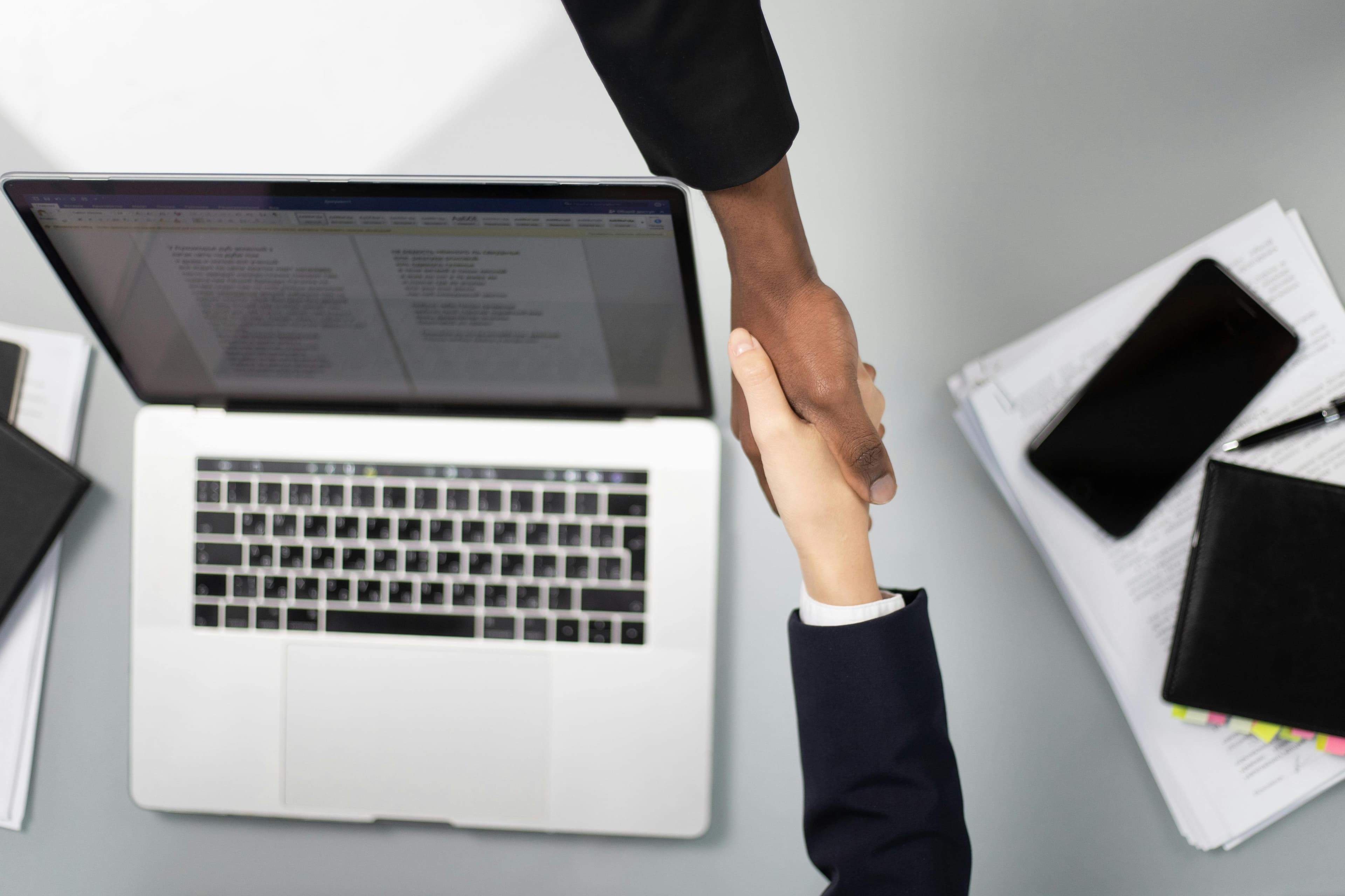 Two people shaking hands over a laptop in an office, representing a business agreement
