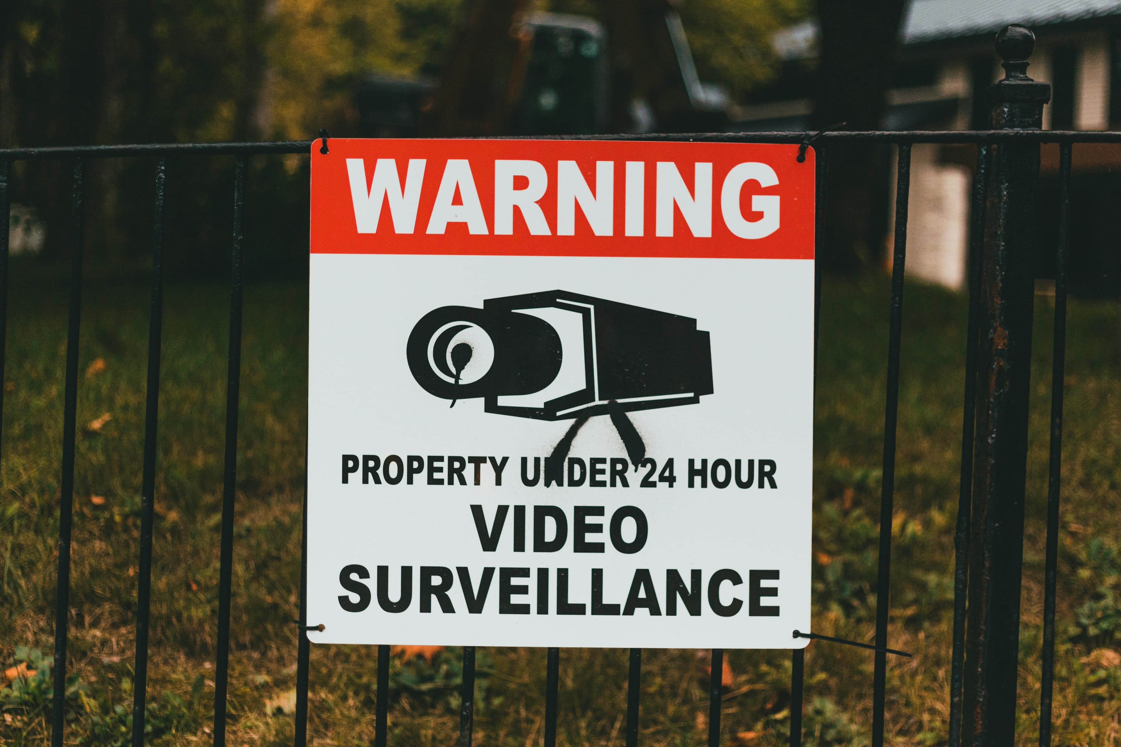 A warning sign on a metal fence indicating monitoring and security