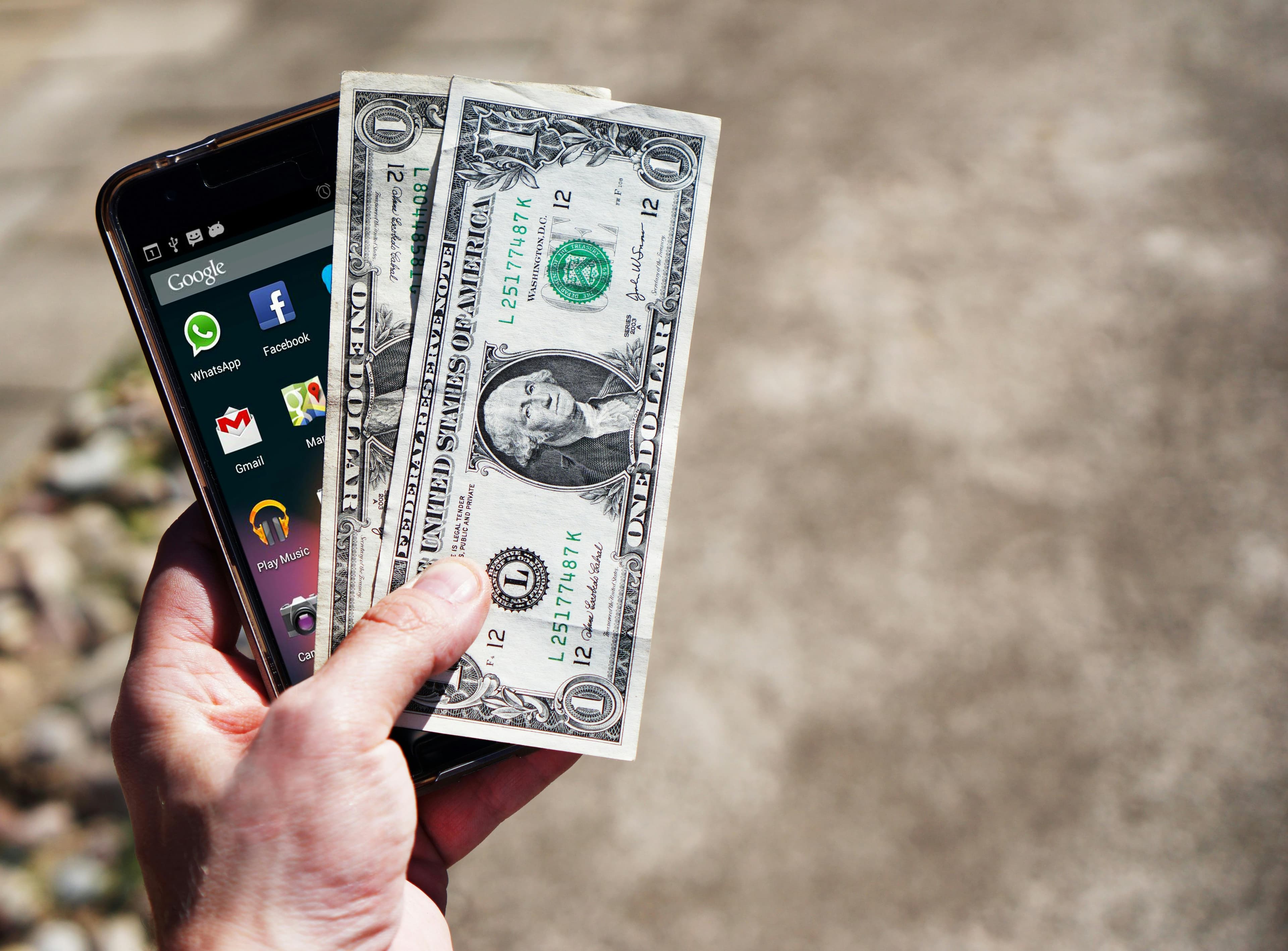 A hand holding a smartphone and US dollar bills