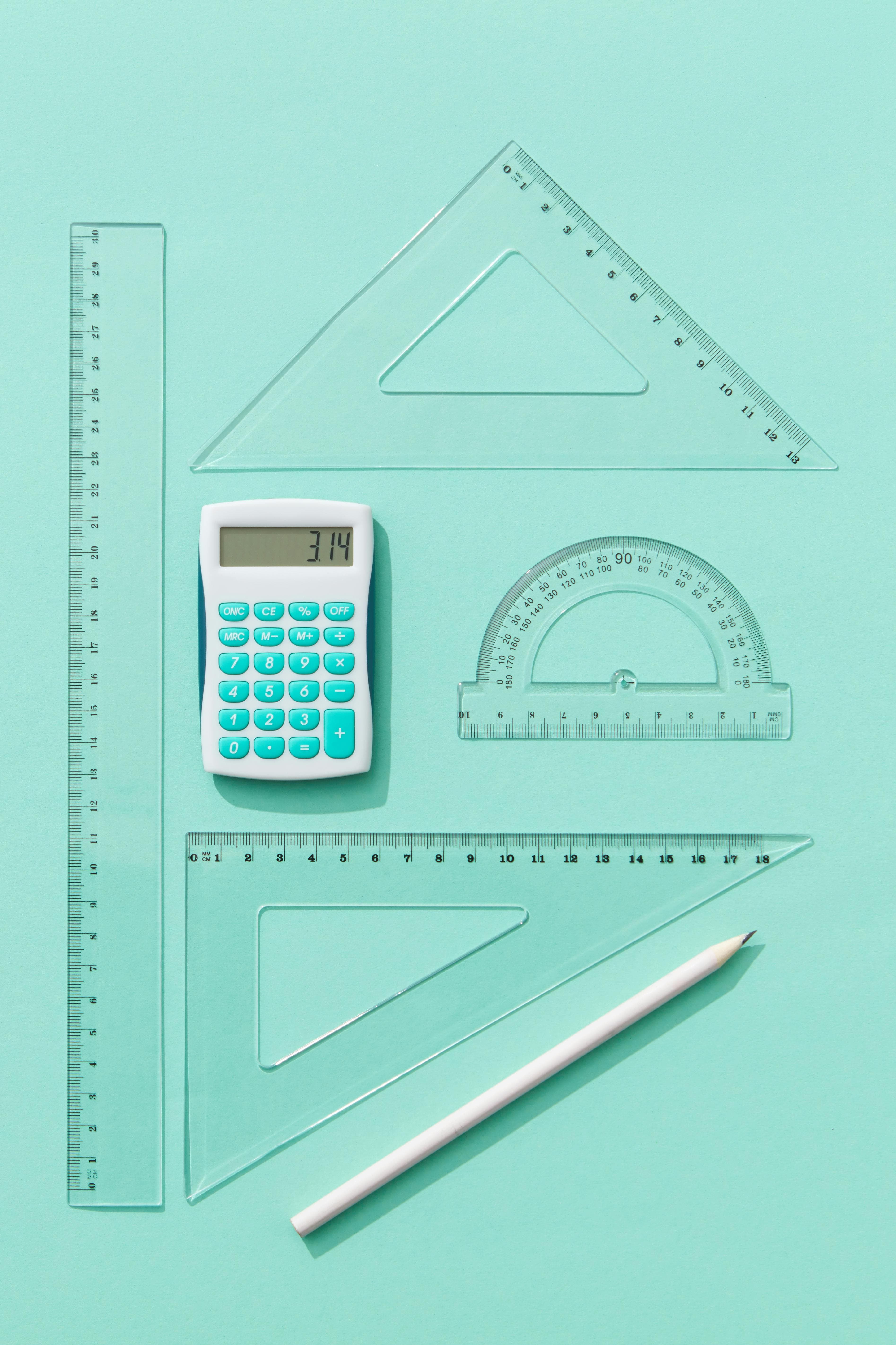 A calculator, pen, and rulers arranged on a teal background